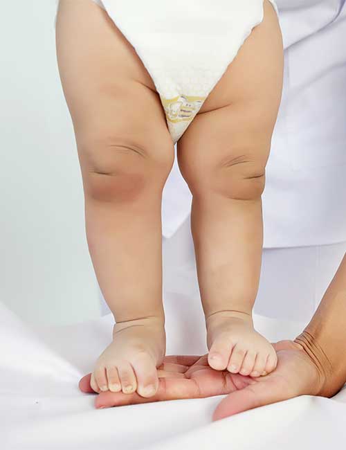 Babyosteopathie in Unna: Osteopath hält sanft die Füße eines stehenden Säuglings, Symbol für sicheres Wachstum und Entwicklung. Kinderosteopathie, Säuglingsosteopathie und Osteopathie für Babys in Unna.